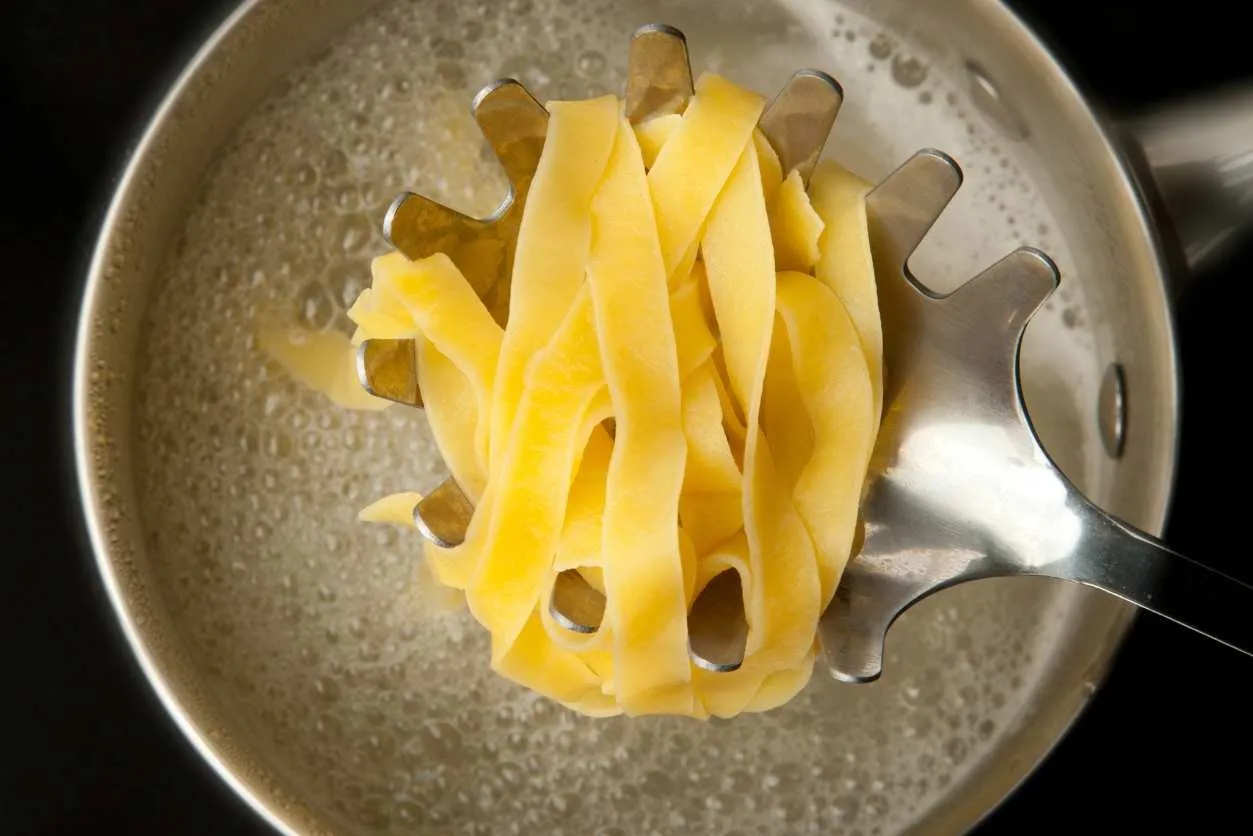 Fresh tagliatelle just drained with a slotted spoon over the cooking pot