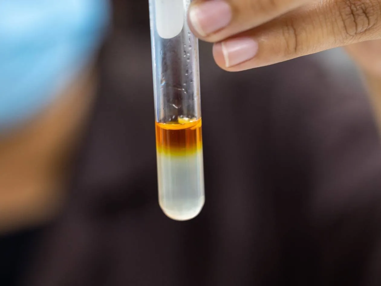 A hand holds a test tube with an amber liquid in a laboratory