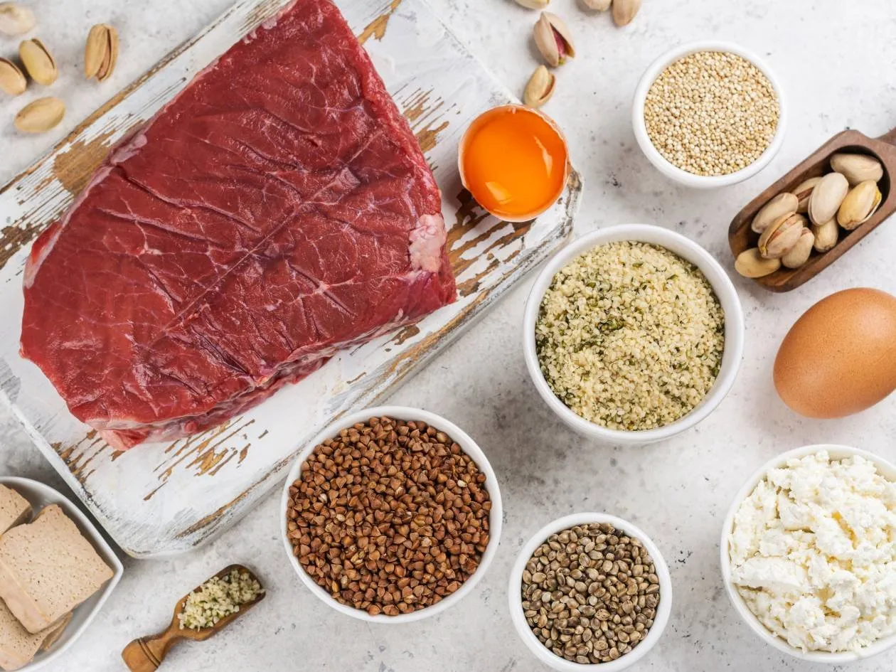Beef fillet surrounded by bowls of legumes, seeds, fresh cheese, an egg and nuts