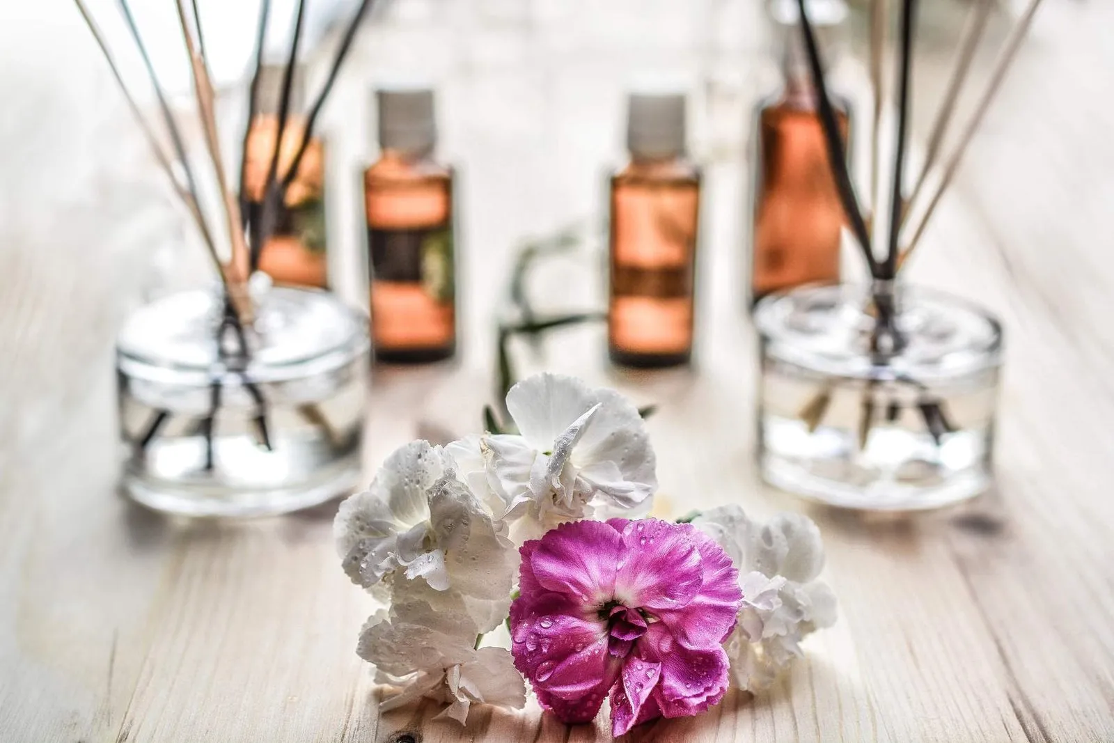 Reed diffusers with essential oil bottles and dried flowers on a light wooden table