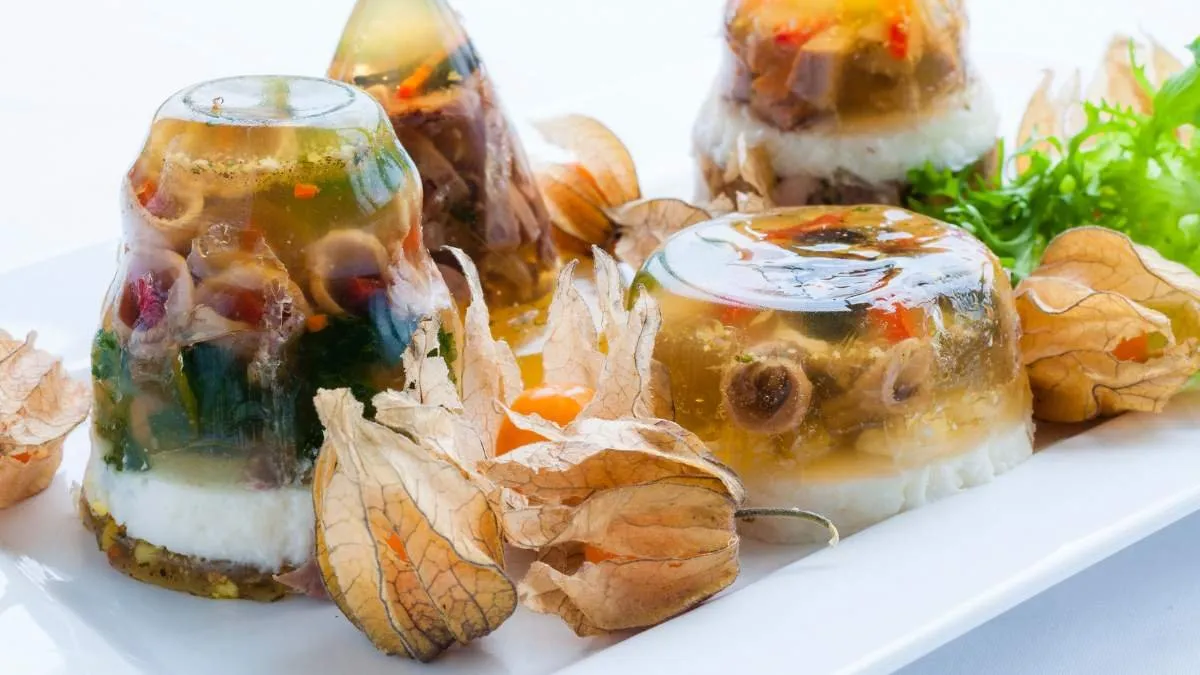 Small jars of aspic with vegetables and fruit in clear gelatine, served on a white tray