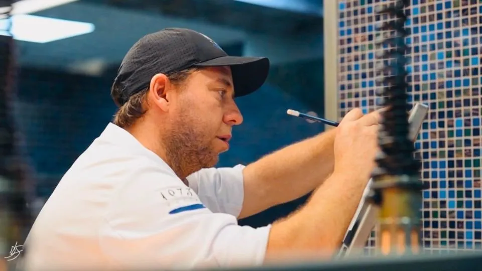 Chef Diego Schattenhofer, in a white chef’s jacket and cap, taking notes in the kitchen