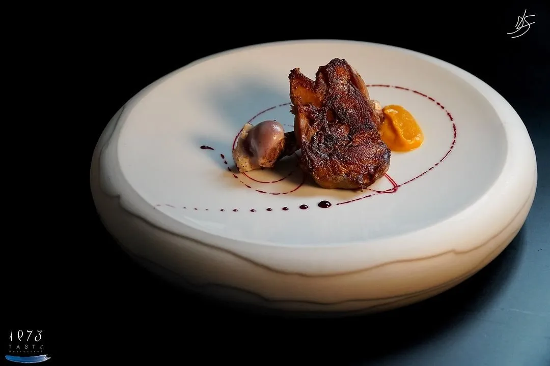 Golden piece of meat with orange purée and sauce trails on a white plate