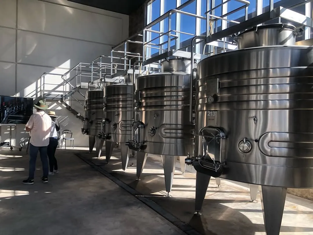 Tanques cilíndricos de acero en una bodega, con válvulas y tuberías, donde fermenta el mosto