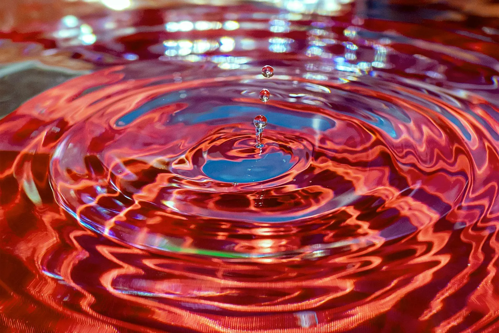 A drop falls onto a sheet of red water and raises concentric ripples