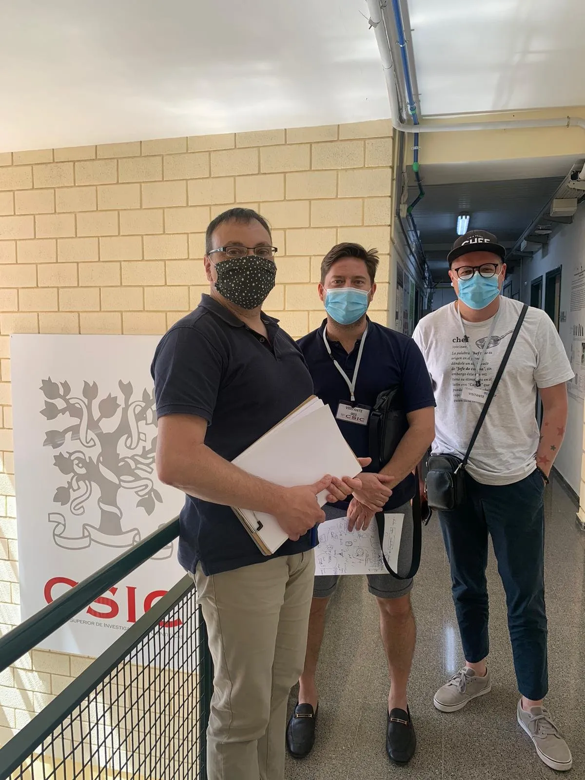 Three men in face masks next to a CSIC sign in a corridor of the centre