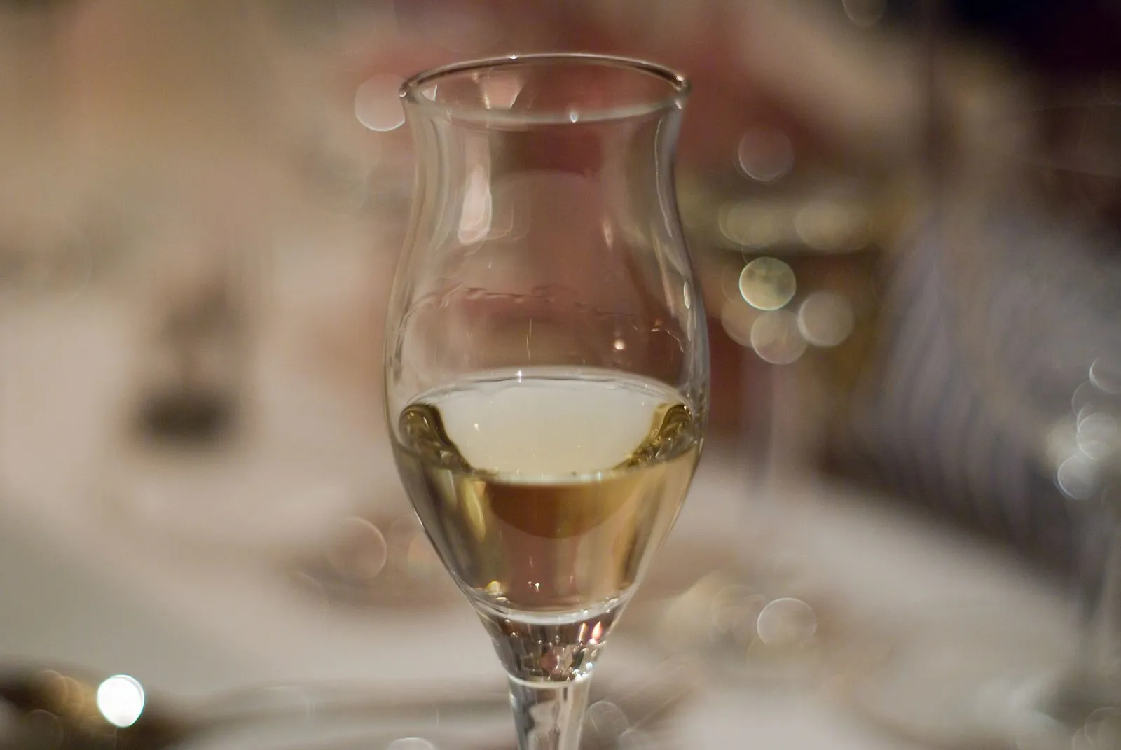 Glass of grappa served on a table, with the restaurant dining room blurred in the background