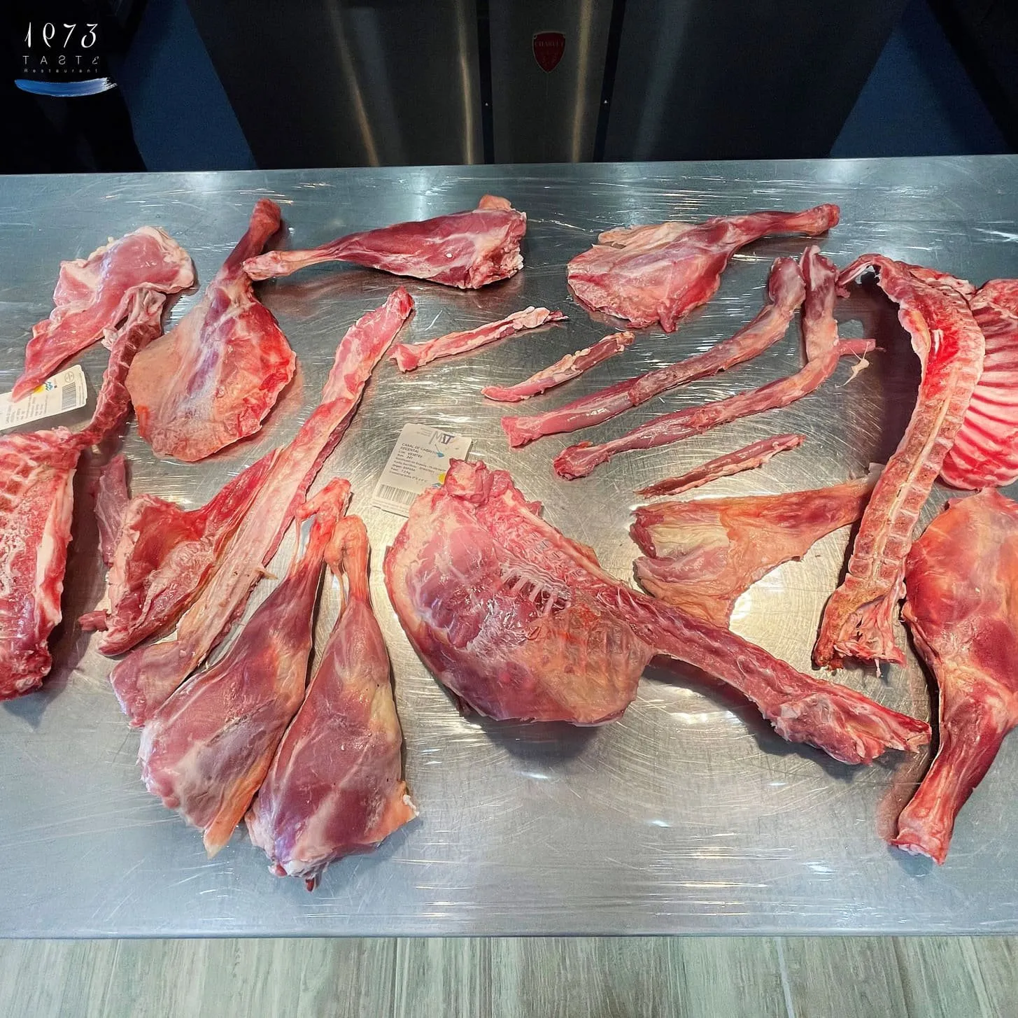 A whole goat, fully butchered, laid out on the steel table of the prep kitchen