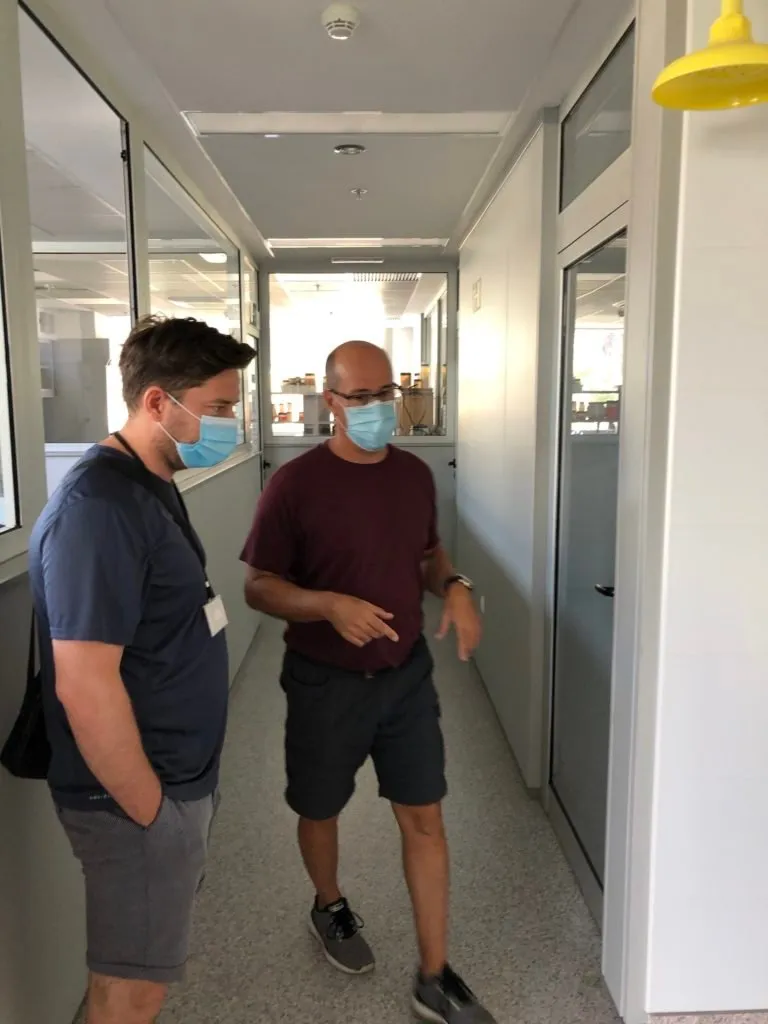 Two men wearing face masks talk in a laboratory corridor at the Spanish Institute of Oceanography