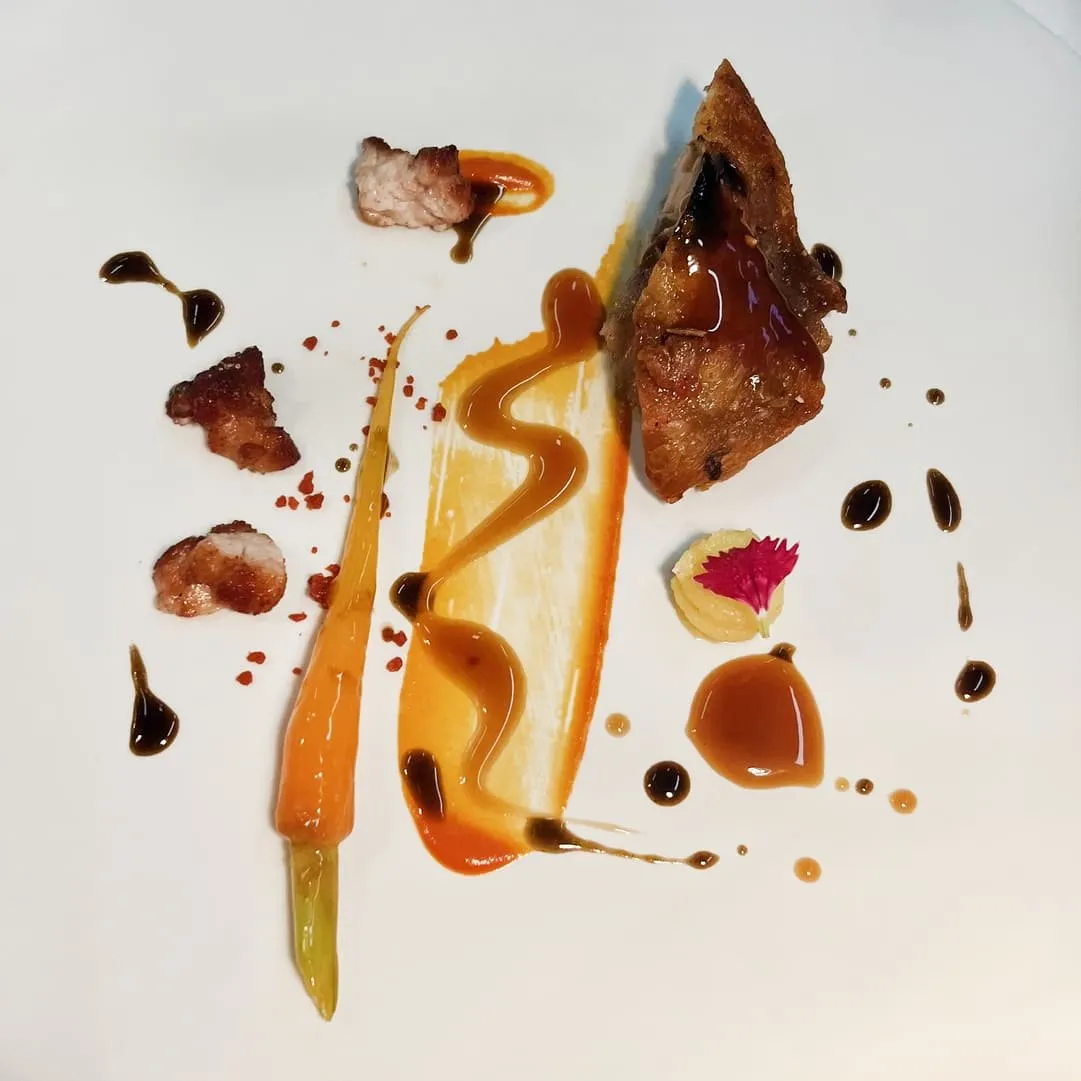 Plated dish of matured goat meat, sauces, carrot and an edible flower