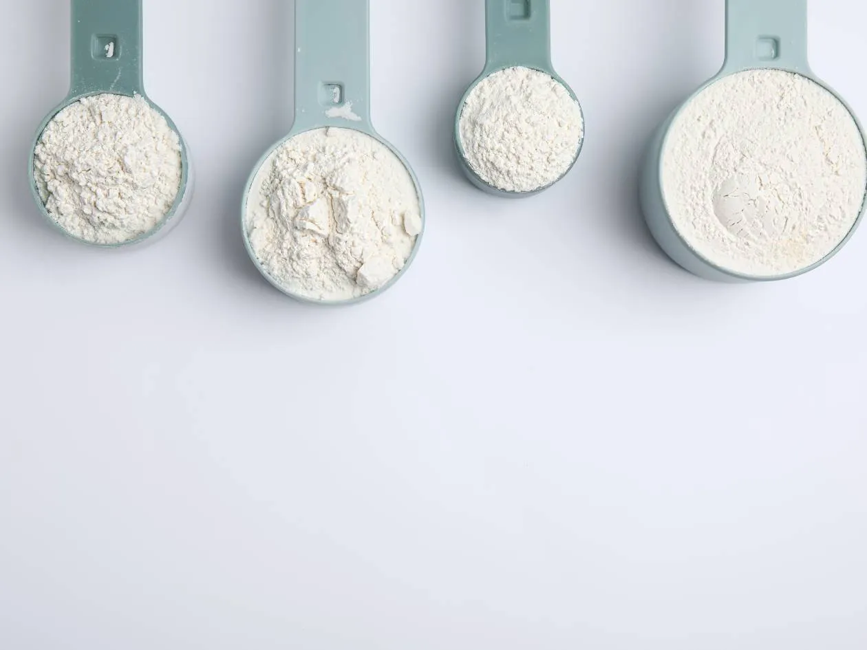 Four measuring spoons with different protein powders on a light background
