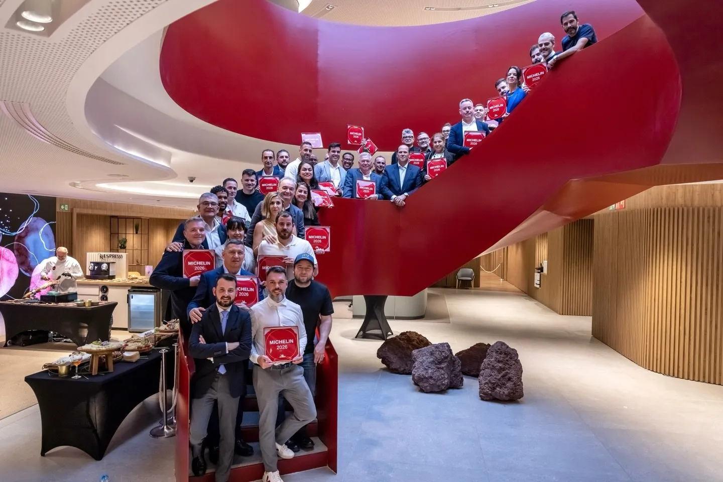 Foto de familia del acto: decenas de responsables de restaurantes posan en la escalera roja del centro «all in one» Gran Canaria sosteniendo sus placas MICHELIN 2026