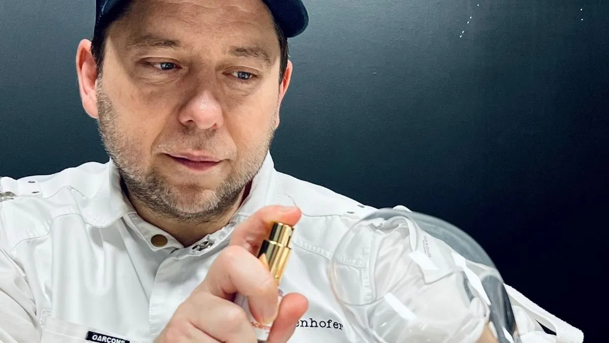 Diego Schattenhofer looking at a golden bottle of edible perfume in his white chef’s jacket