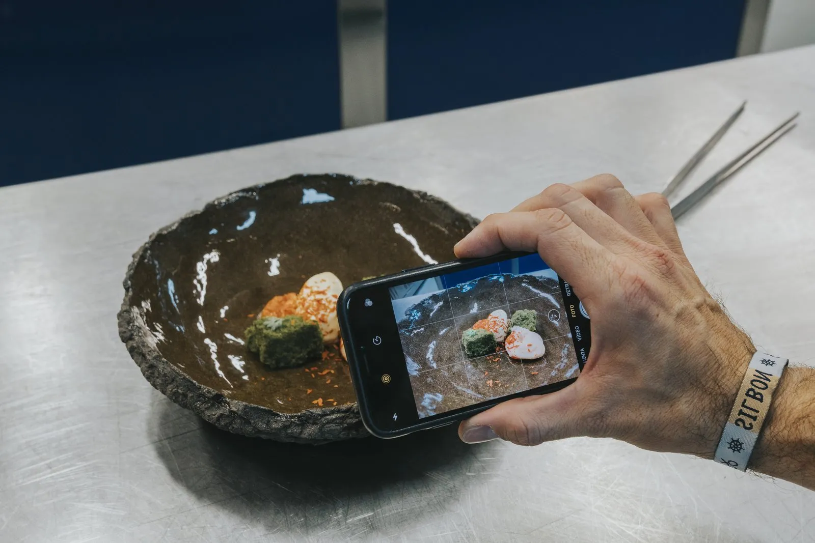 Dłoń trzyma telefon w poziomie i fotografuje danie podane w misie z ciemnego kamienia