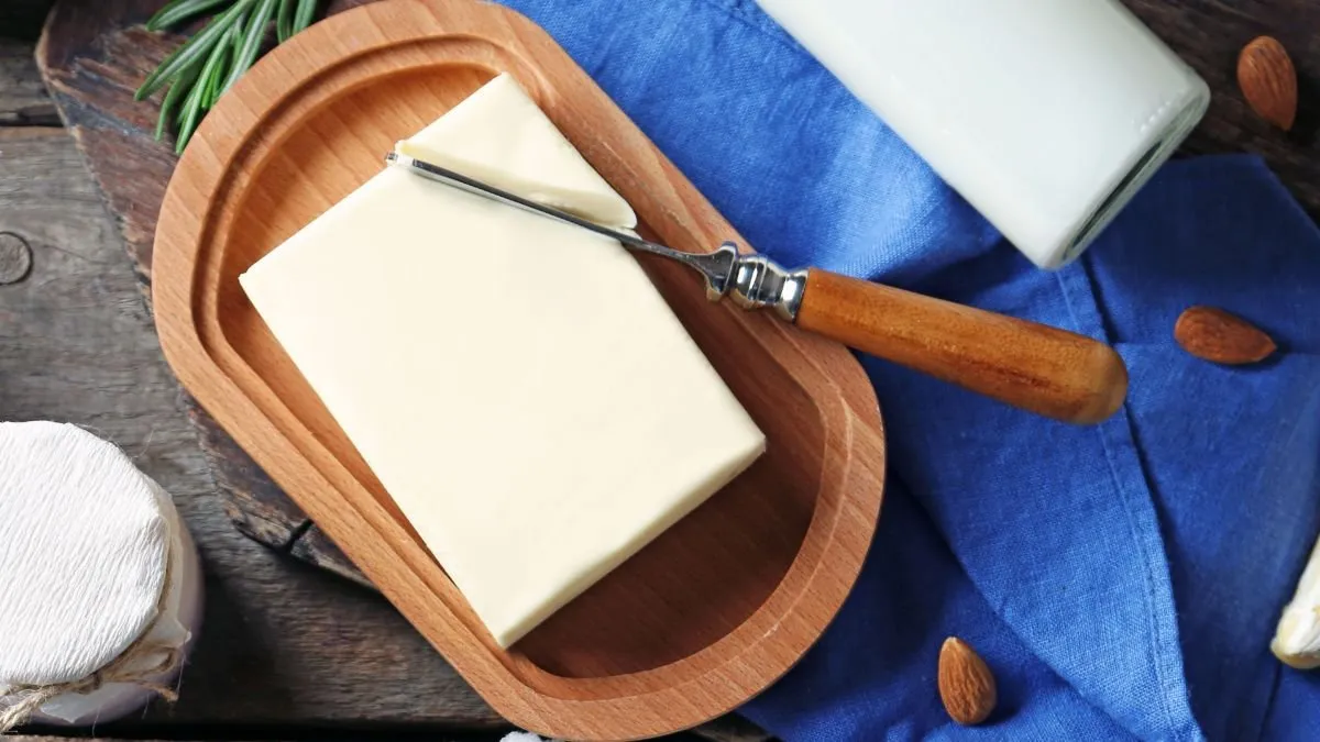 Block of goat butter on a wooden tray with a knife, milk and almonds