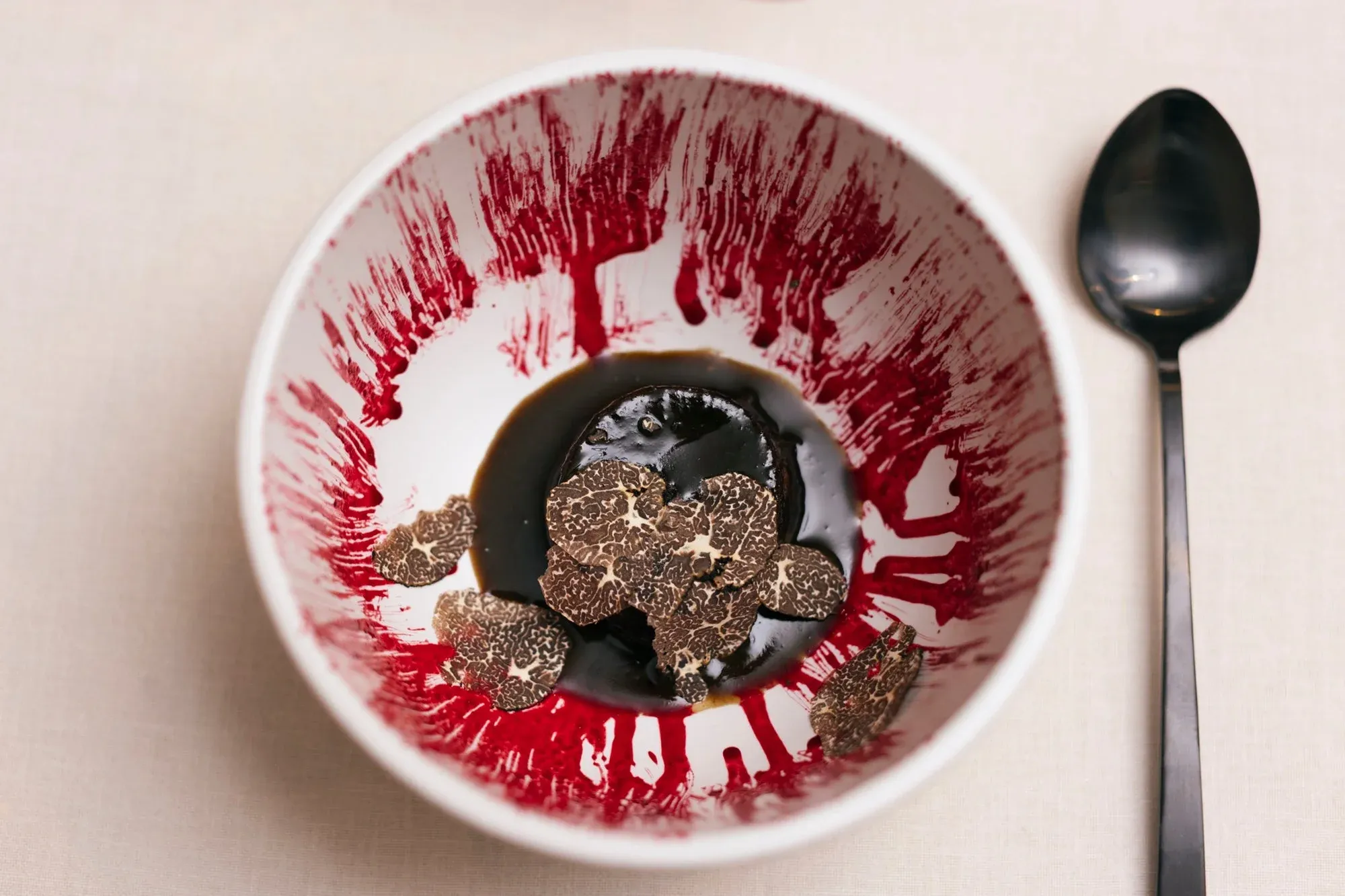 Royale of Canarian black pig with truffle shavings in a red-veined bowl