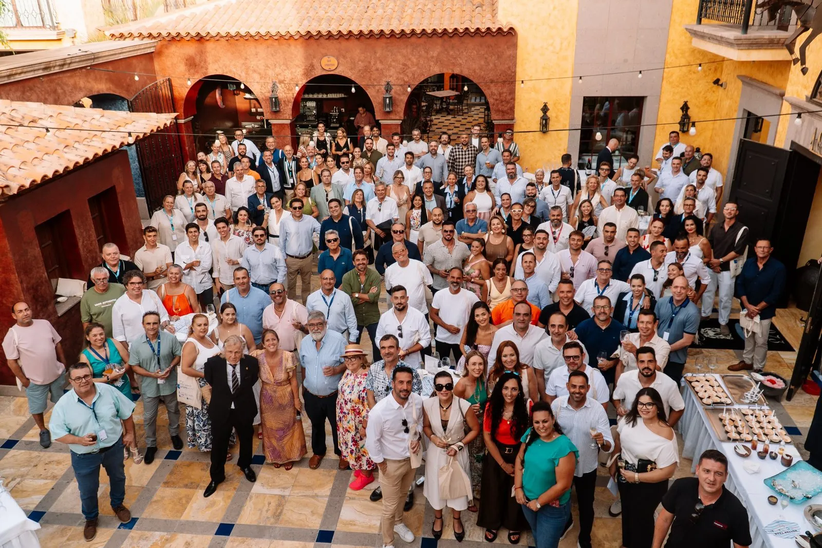 Más de un centenar de invitados posan juntos en el patio del Hotel Villa Cortés, bajo los arcos y las fachadas ocres del hotel, con una mesa de aperitivos a un lado