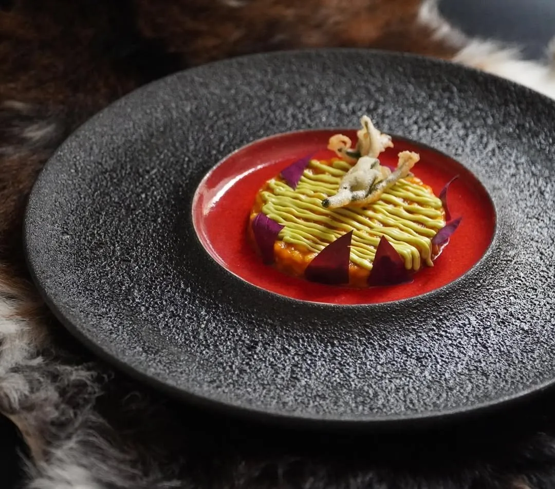 Plate of matured goat with green cream on a red sauce base