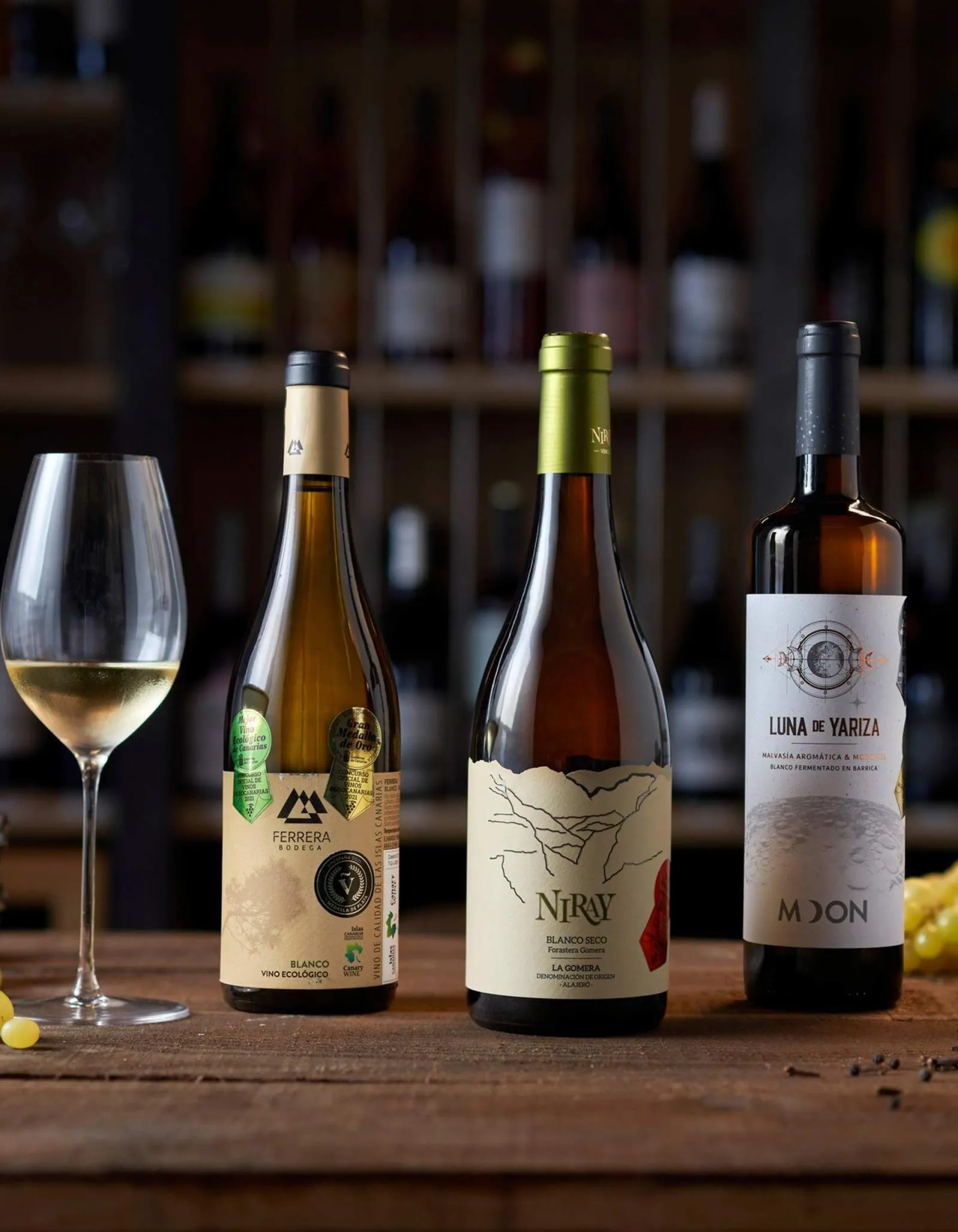 Three bottles of Canarian white wine and a glass poured on a wooden table