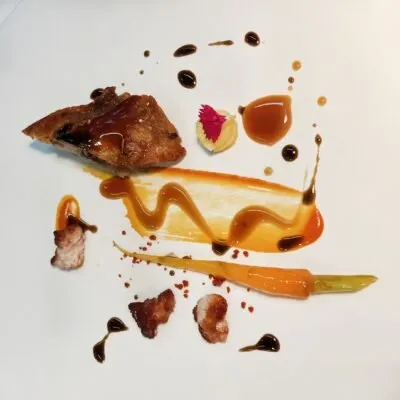 Plate of matured goat with glazed carrot and sauces on white porcelain