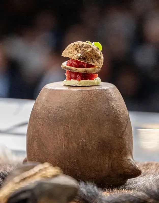 Bite-sized meat tartare on a bread roll served on a piece of carved wood