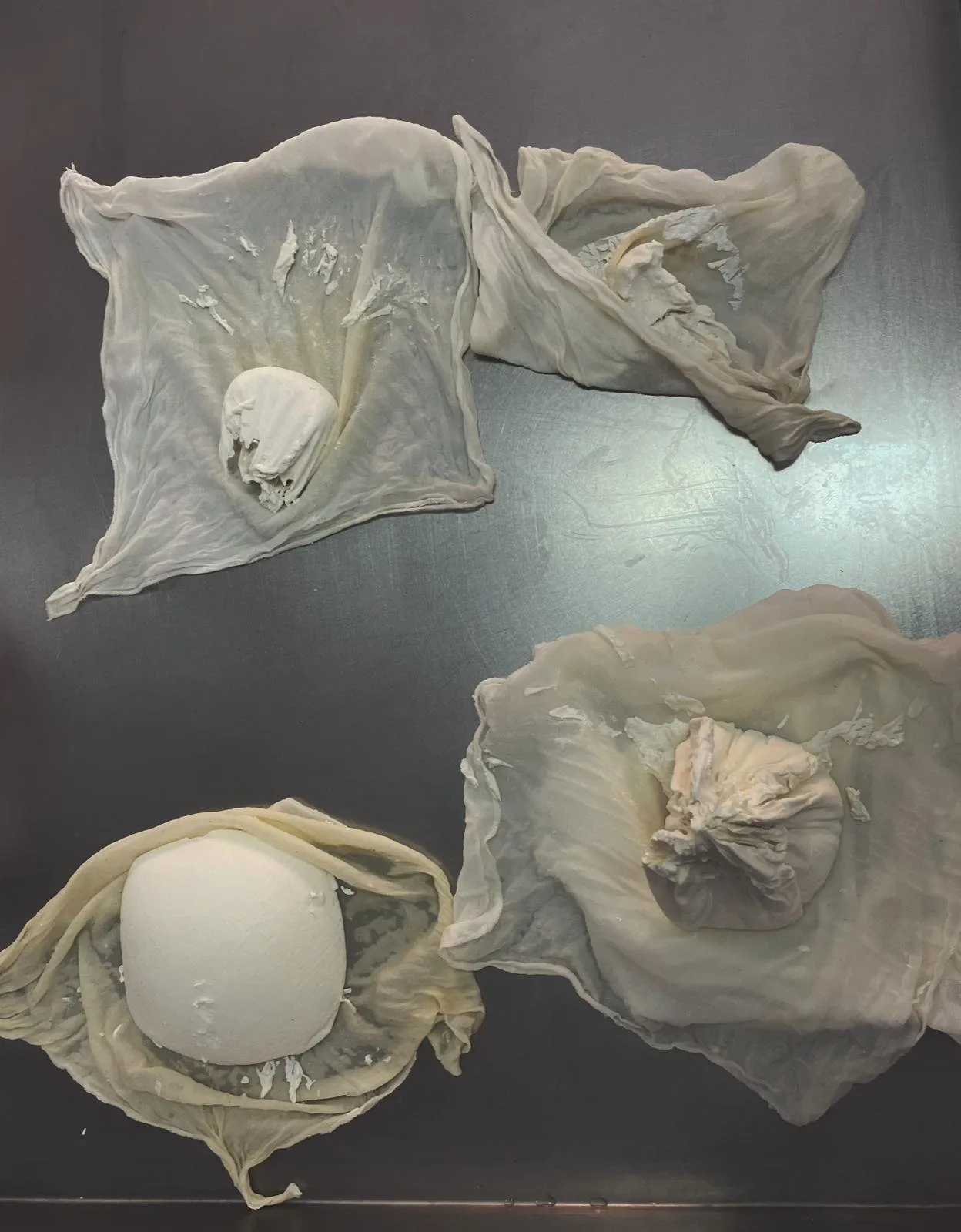Three pieces of curd wrapped in cloths on the steel table