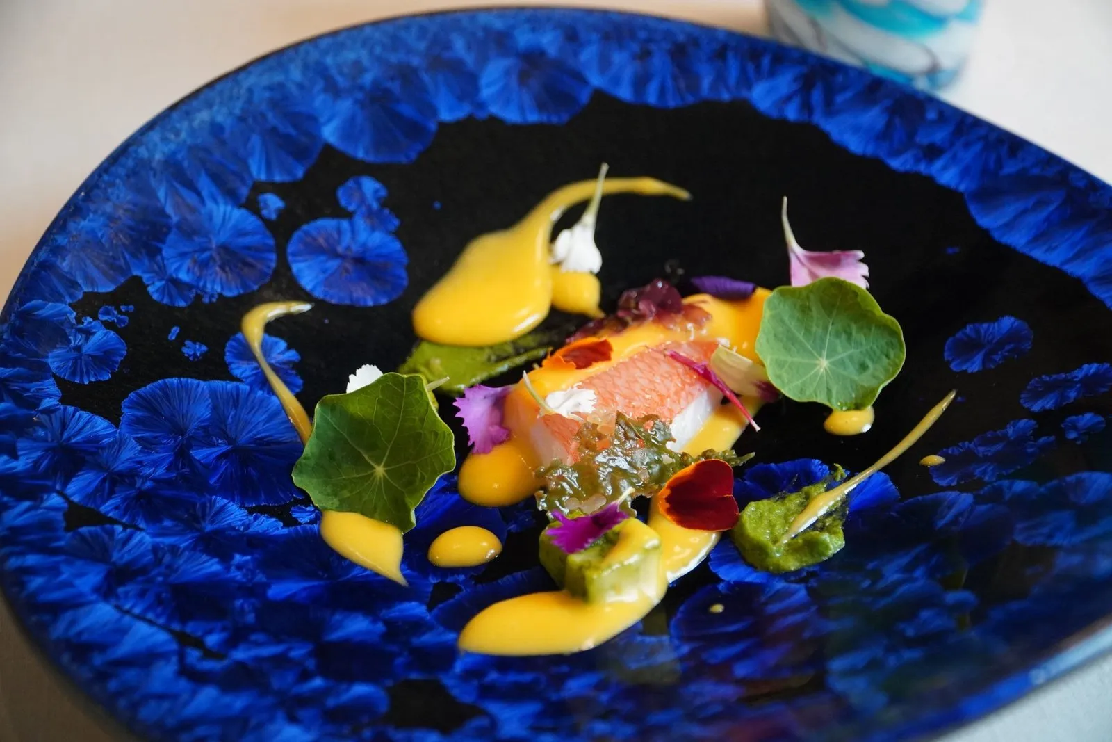 Fish loin with a yellow emulsion and edible flowers on a blue plate