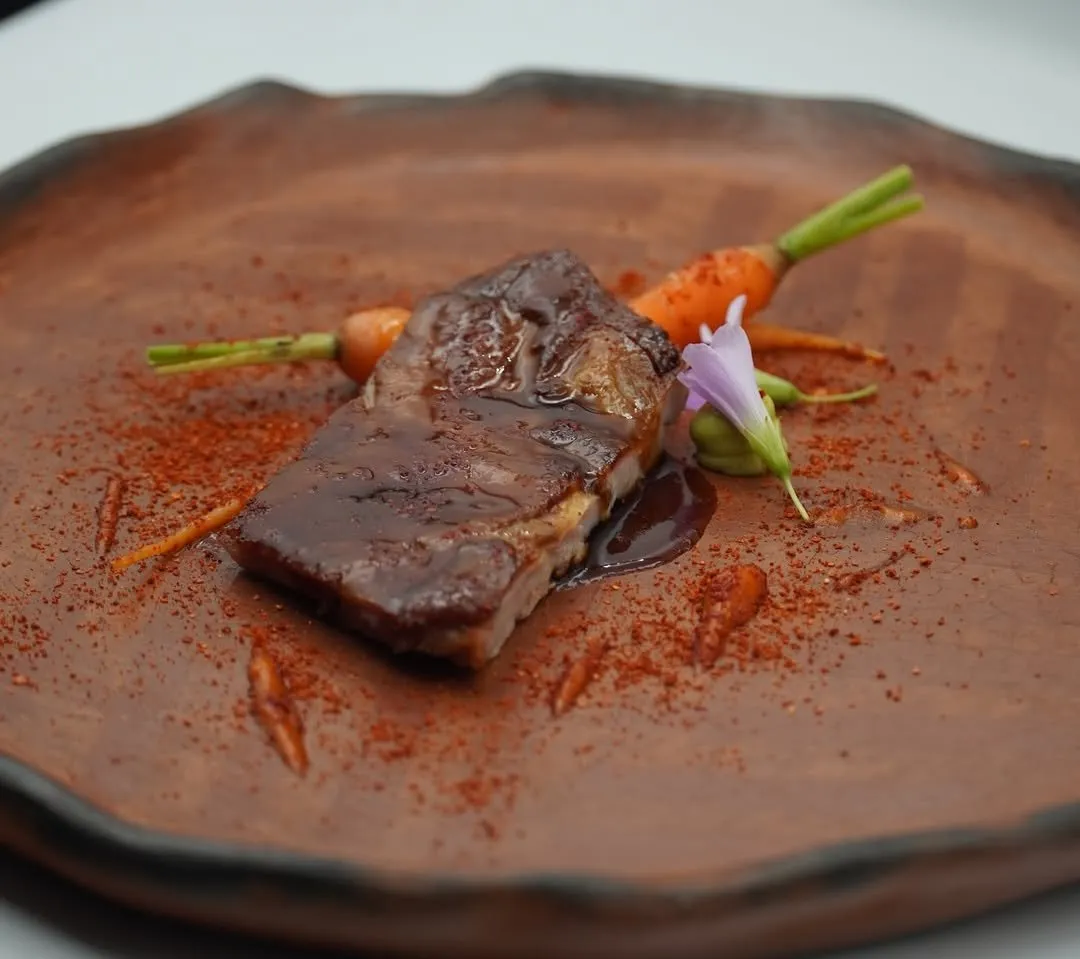 Glazed piece of matured goat with baby carrots and an edible flower