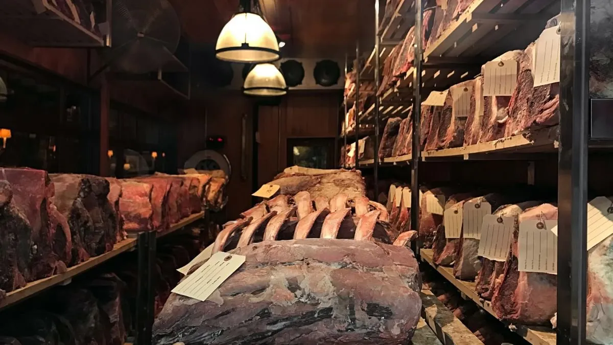 Dry-ageing room with large labelled cuts of beef on wooden shelving
