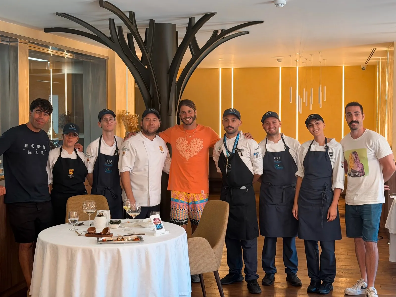 Foto de grupo de nueve personas junto al árbol escultórico de la sala de Taste 1973: la brigada de cocina con gorras y delantales del restaurante y varios miembros del equipo de rodaje, uno con camiseta de «ECOS DEL MAR»