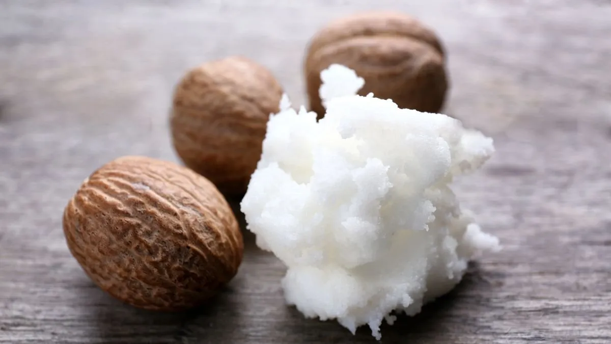 Portion of goat butter next to three brown-shelled nuts on wood