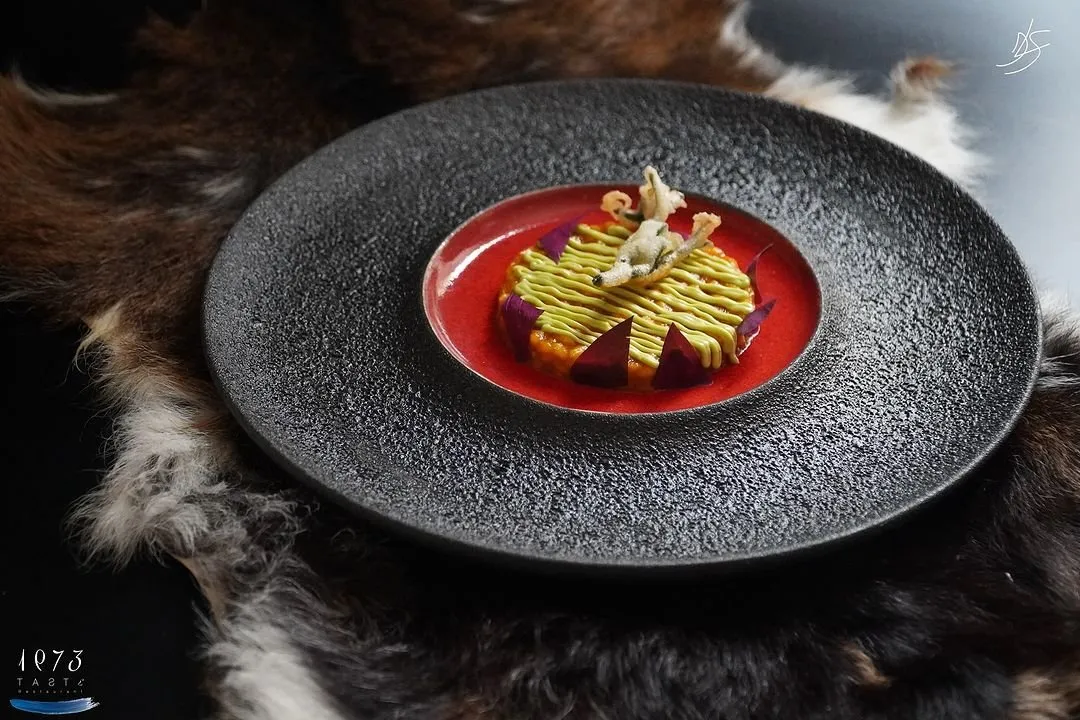 Black plate with a yellow preparation over red sauce served on a goat hide