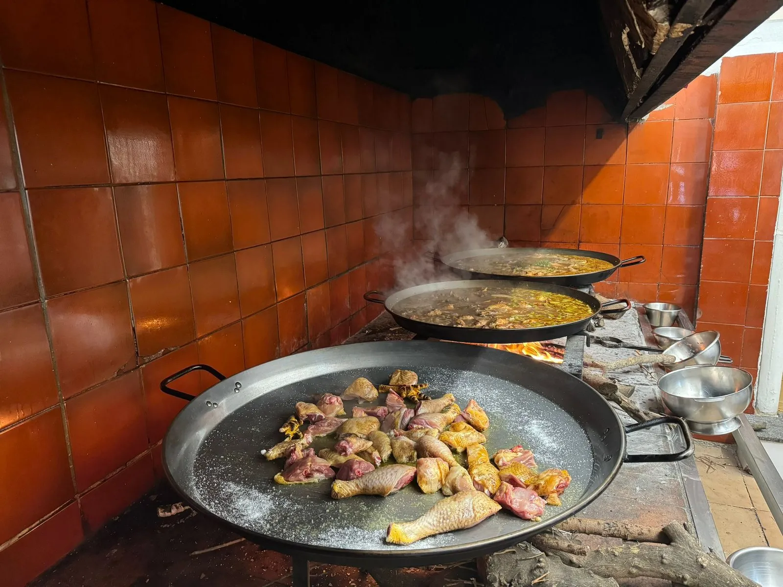 Three paellas over a wood fire in a kitchen with red tiles