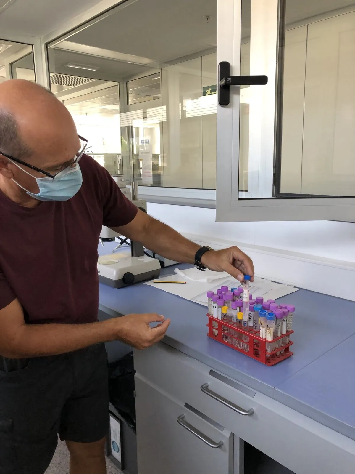Researcher wearing a face mask places a tube in a red laboratory rack