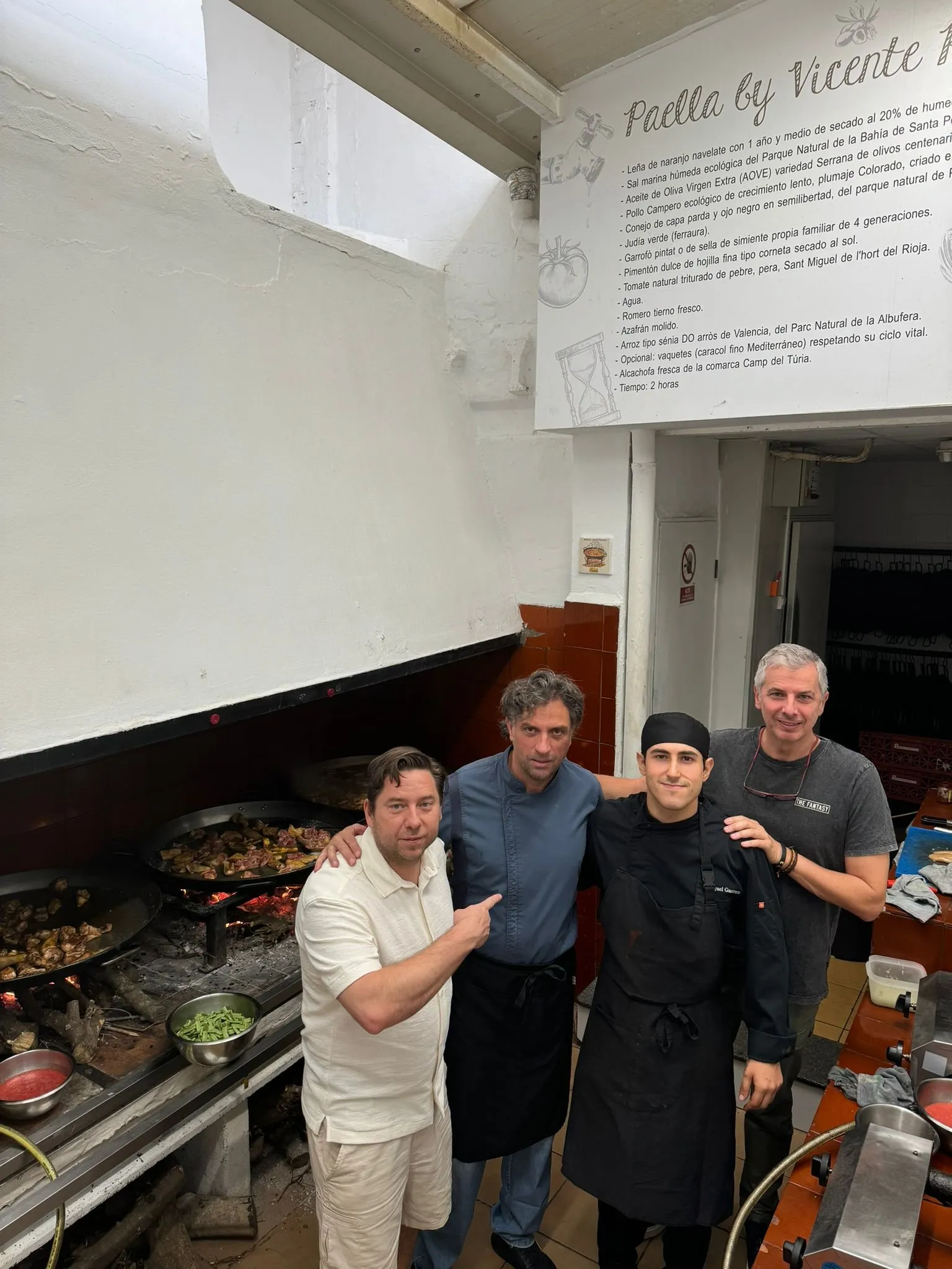Four cooks pose beneath the sign with Vicente Rioja’s paella recipe