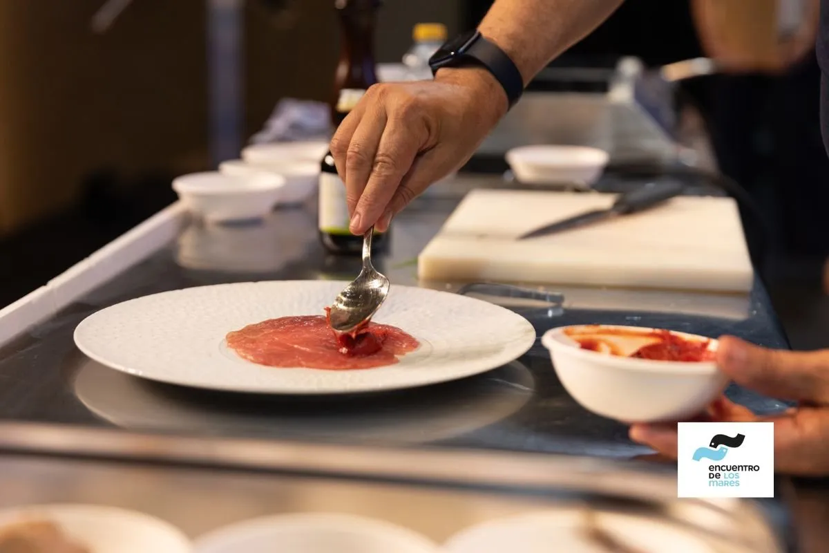 A cook uses a spoon to nappe a thin sheet onto a white plate