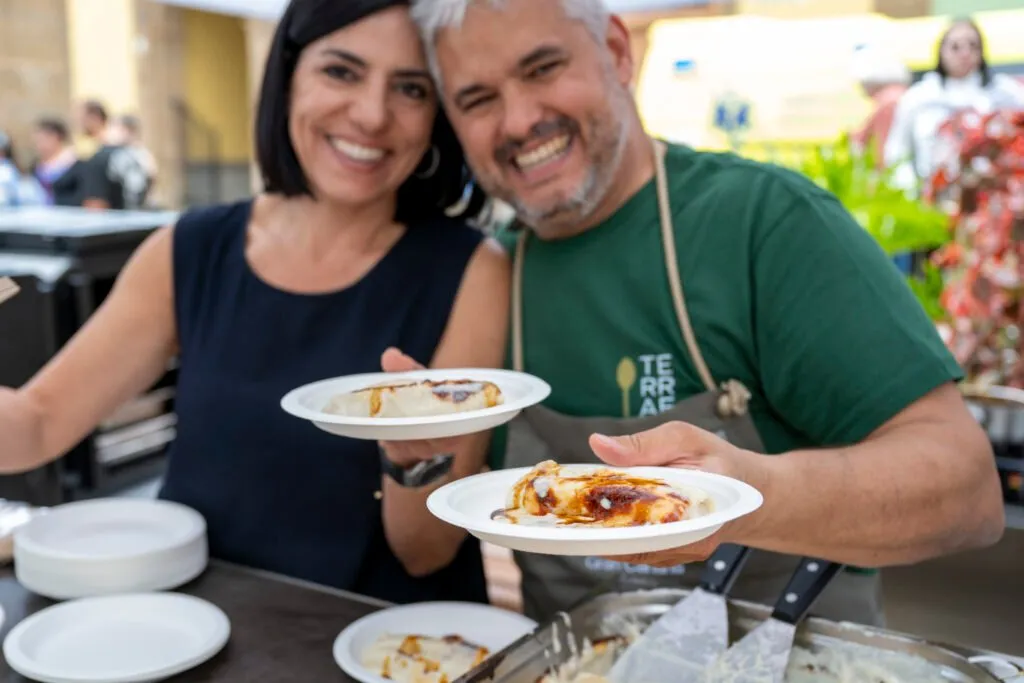 Two cooks, a woman and a man, come out of the stall smiling with two plates in hand