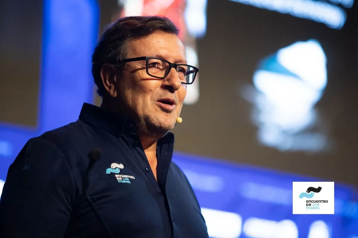 Speaker with glasses and a microphone presenting in front of the congress screen