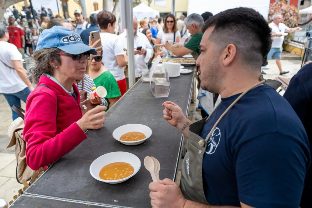 Two attendees standing and tasting a stew served in a bowl, spoon in hand