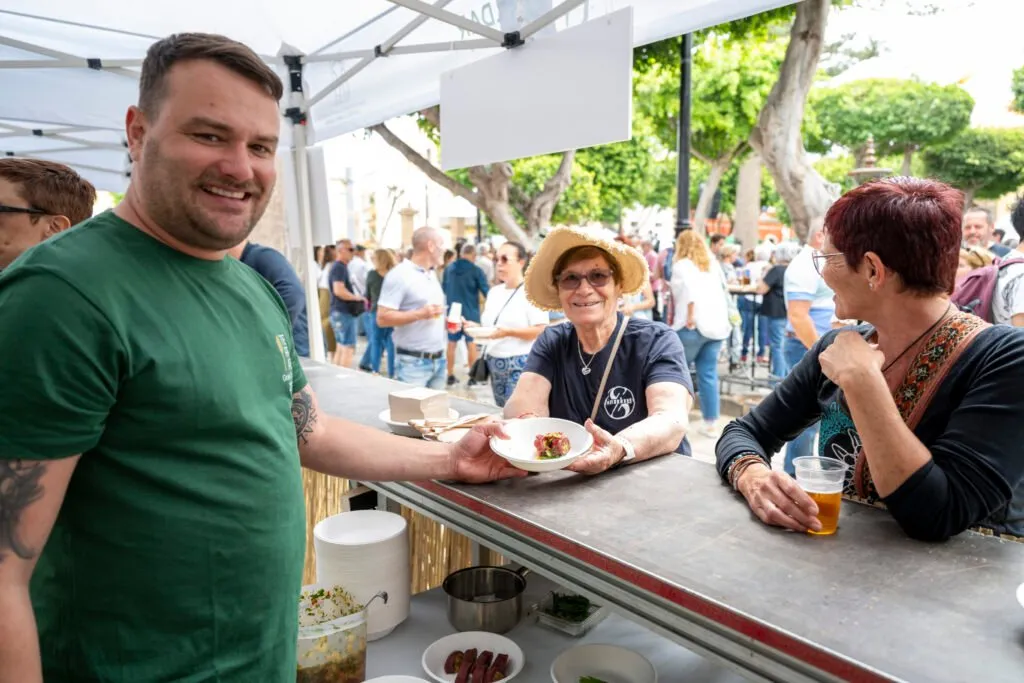 A chef hands a plate to two attendees over the stall counter