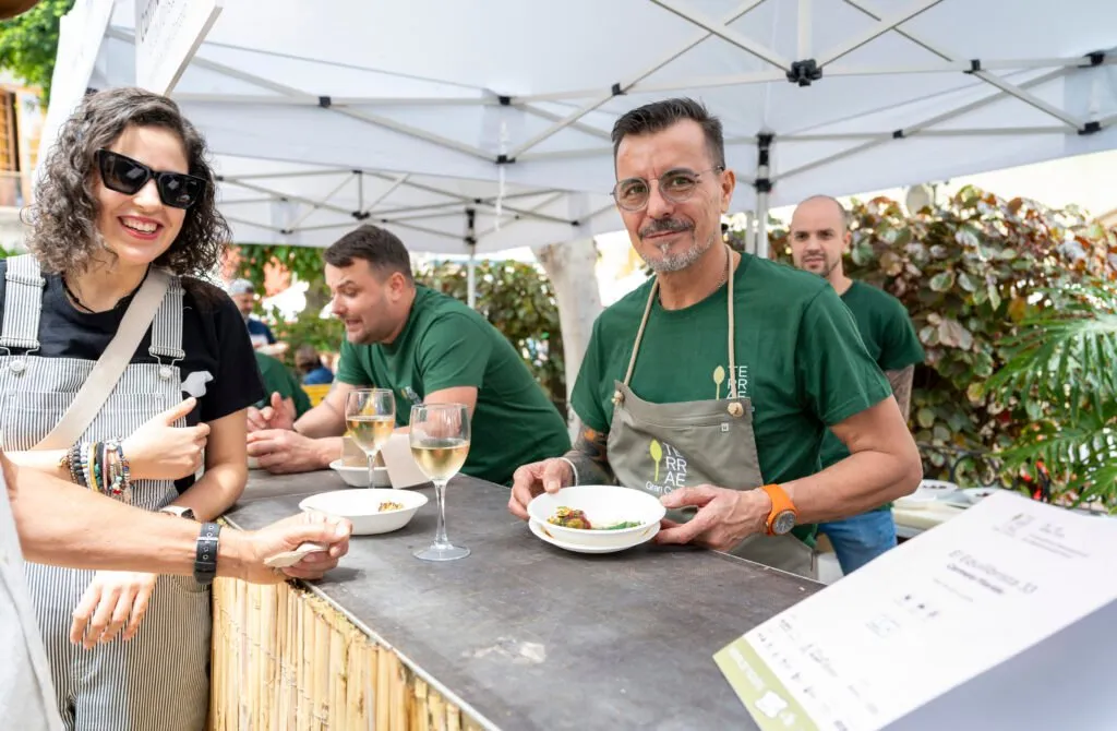 An attendee collects her plate as two chefs tend to the counter