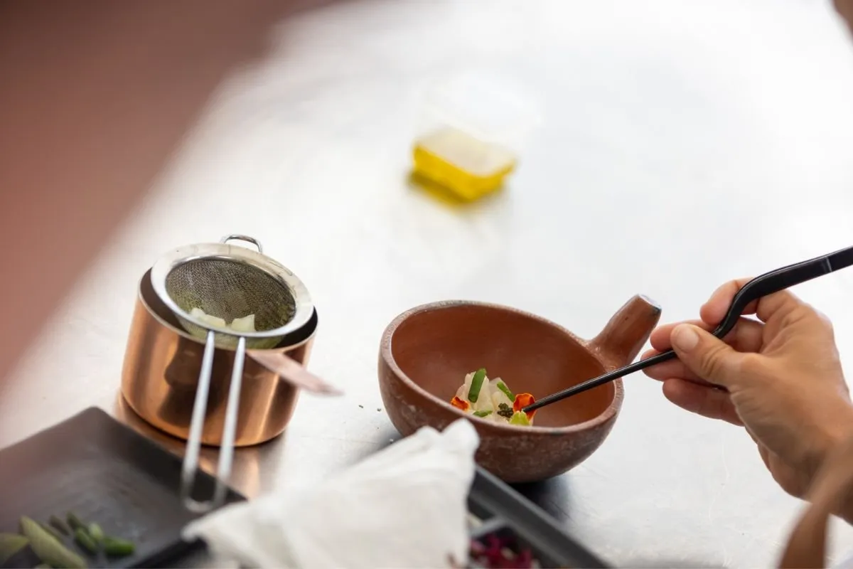 Plating with tweezers in a clay bowl next to a copper pan
