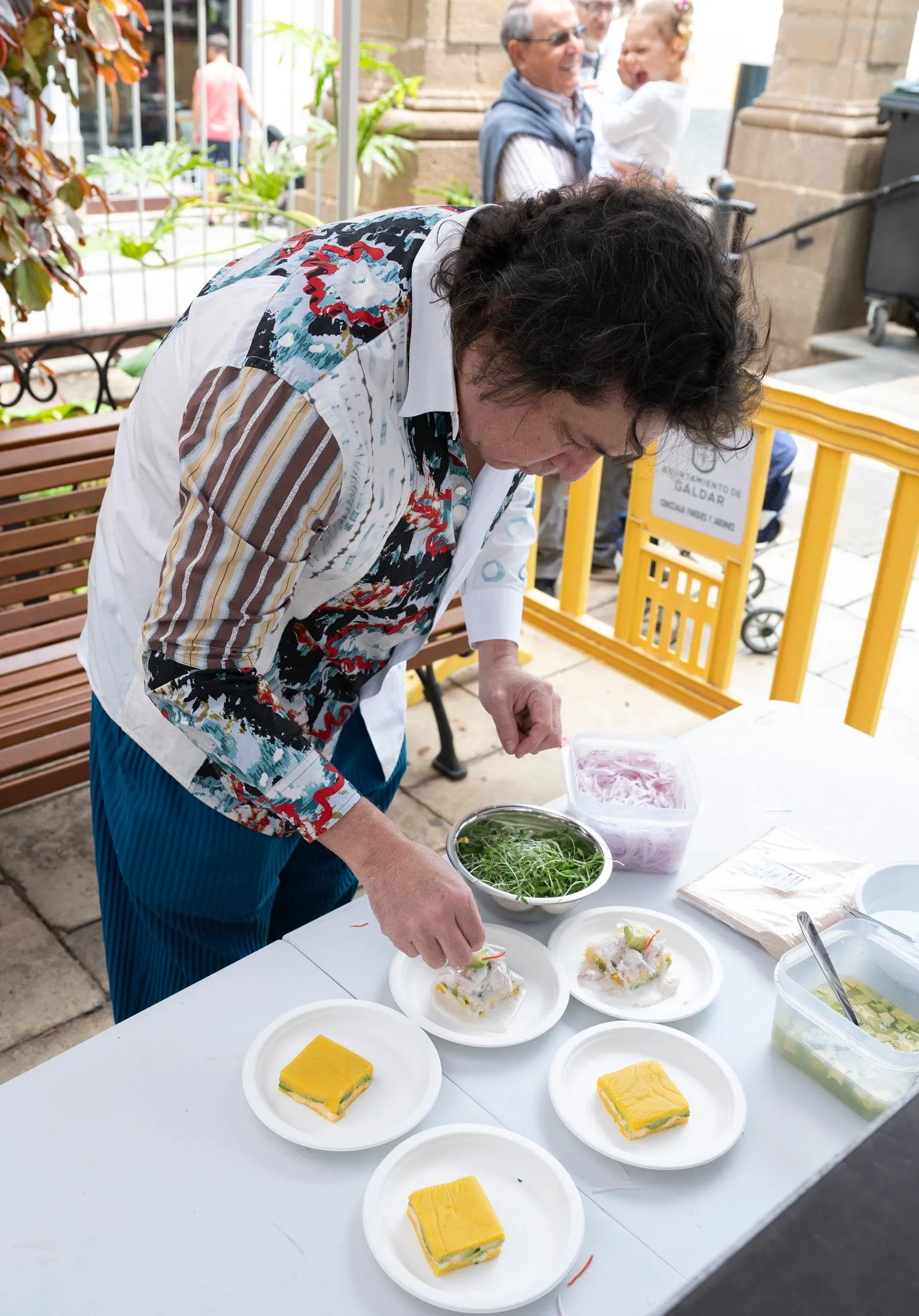 Chef Gastón Acurio finishes four plates lined up on the counter with fresh herbs