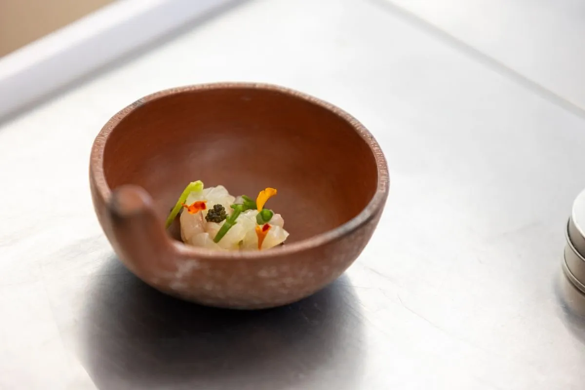 Clay bowl with a dish of fish, vegetables and edible flowers