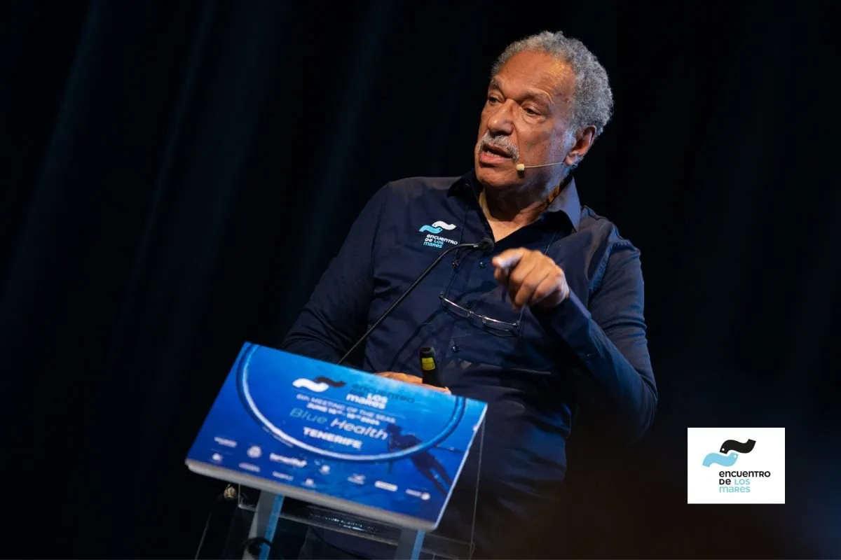 Grey-haired speaker addressing the audience from the lectern of the VI Encuentro de los Mares