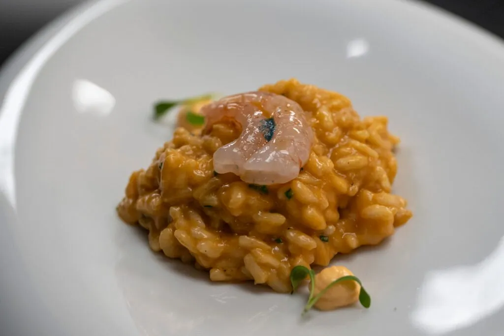 A plate of creamy arroz meloso rice topped with a sliver of fish and shoots