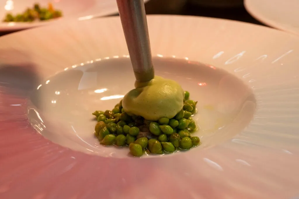 A sauce is poured over a dish of peas and green purée