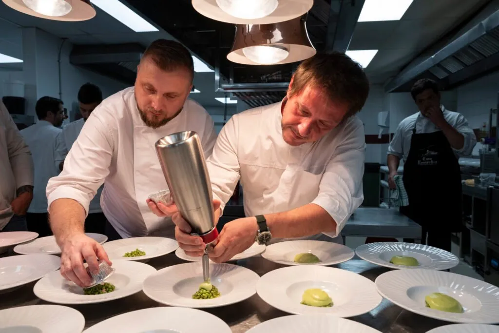 Two chefs plating in a row under the heat lamps of the pass