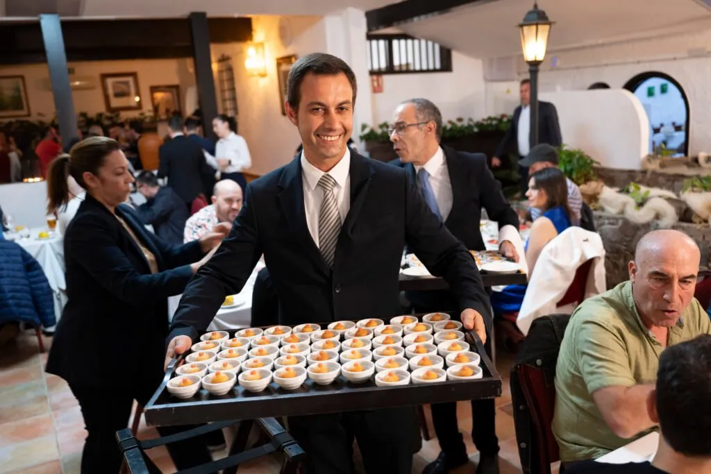 A waiter carrying a tray with dozens of individual portions