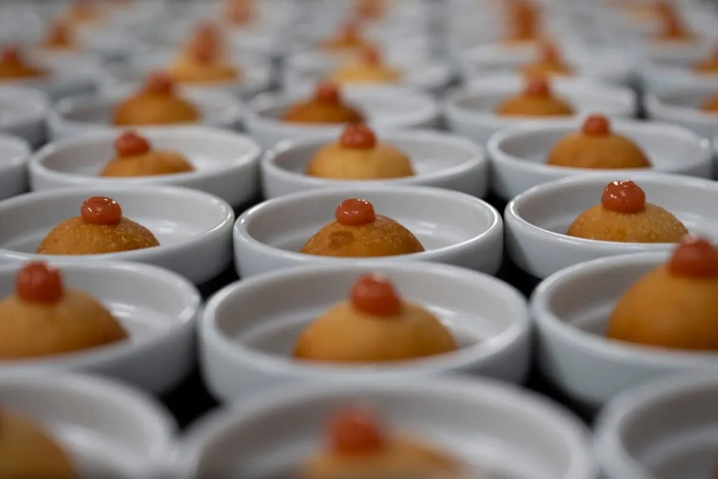 Rows of bowls with a bite-sized dish topped with a dot of red sauce